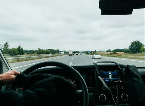 Mains d’un chauffeur sur le volant, route devant le véhicule