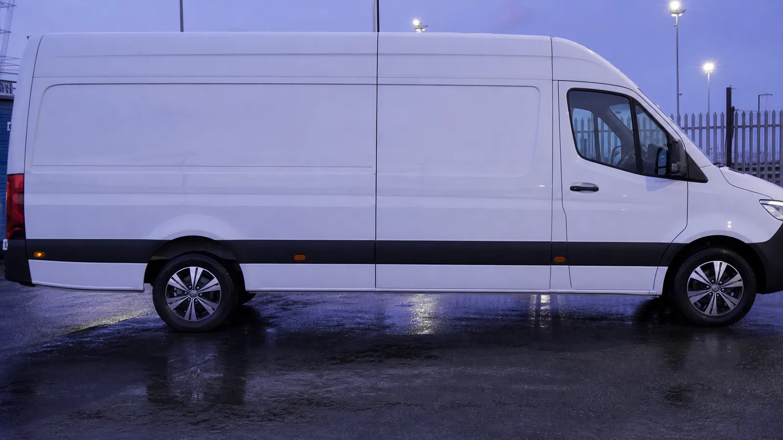 Camionnette utilitaire moderne garée de profil dans une cour d'entreprise éclairée en fin de journée, sans personne à bord